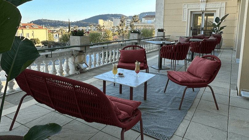 Terrasse avec meubles de jardin rouges, plantes et vue sur la ville par une journée ensoleillée.