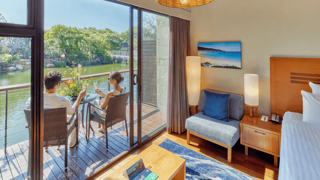Couple enjoying a serene lakeside view from their private balcony with comfortable seating and a cozy bedroom nearby.