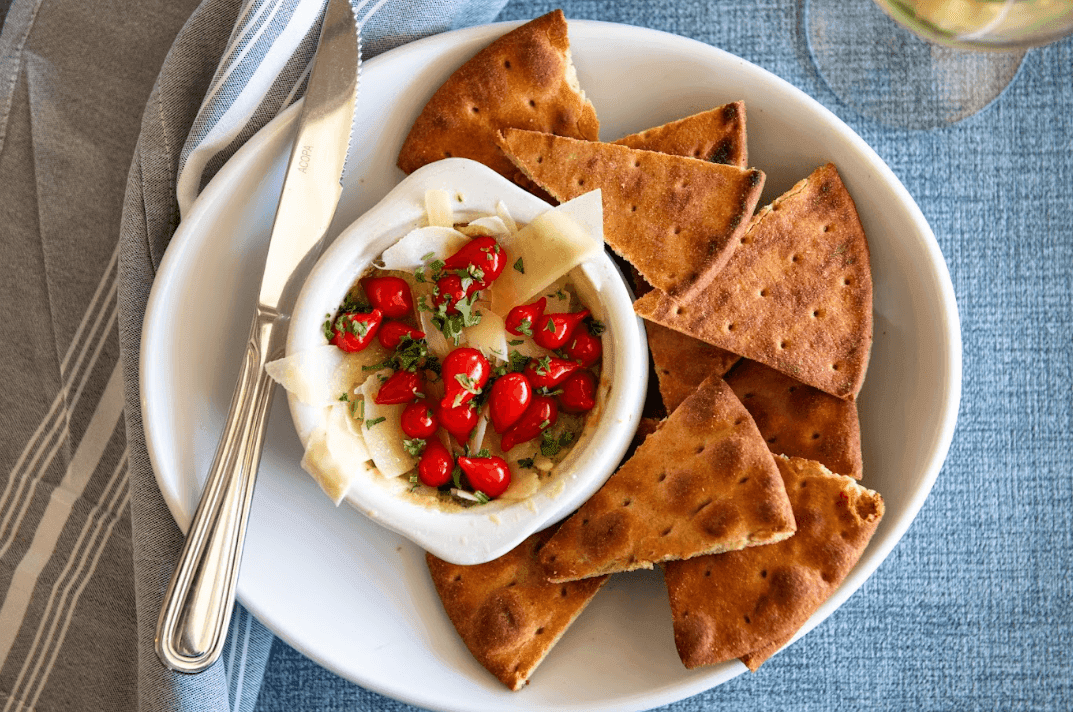 a white bowl of cheese and tomatoes with crackers on a plate