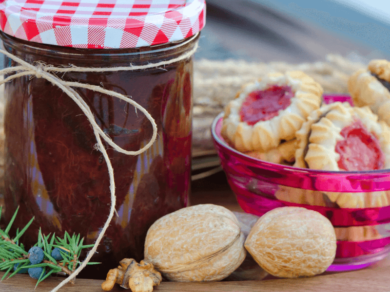 Homemade jam jar with checkered lid beside pink bowl of jam-filled cookies and walnuts at Busselton Foreshore Market.