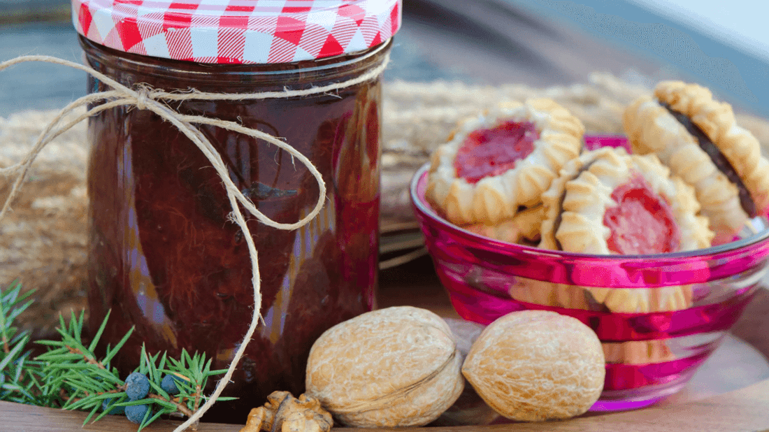 Homemade jam jar with checkered lid beside pink bowl of jam-filled cookies and walnuts at Busselton Foreshore Market.