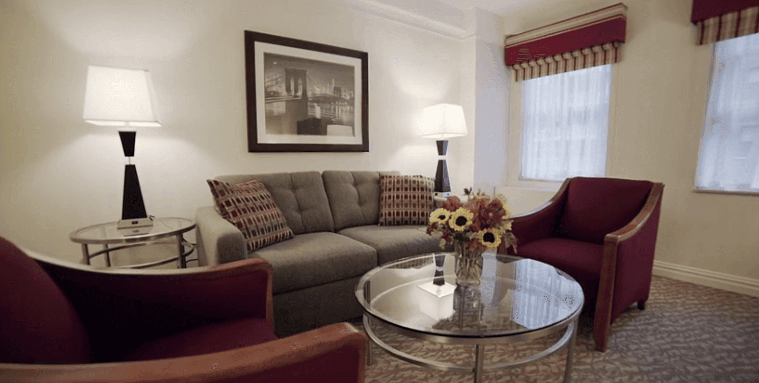 A hotel room with a gray sofa, two red armchairs, a coffee table, and a picture frame on the wall.