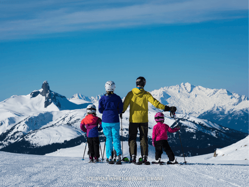 Skier family posing on a snowy pathway with a scenic view near Blackcomb Springs Suites