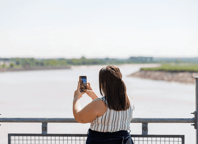 Woman holding a smartphone to photograph the wide mudflat river vista over an observation railing near the Rodd Moncton