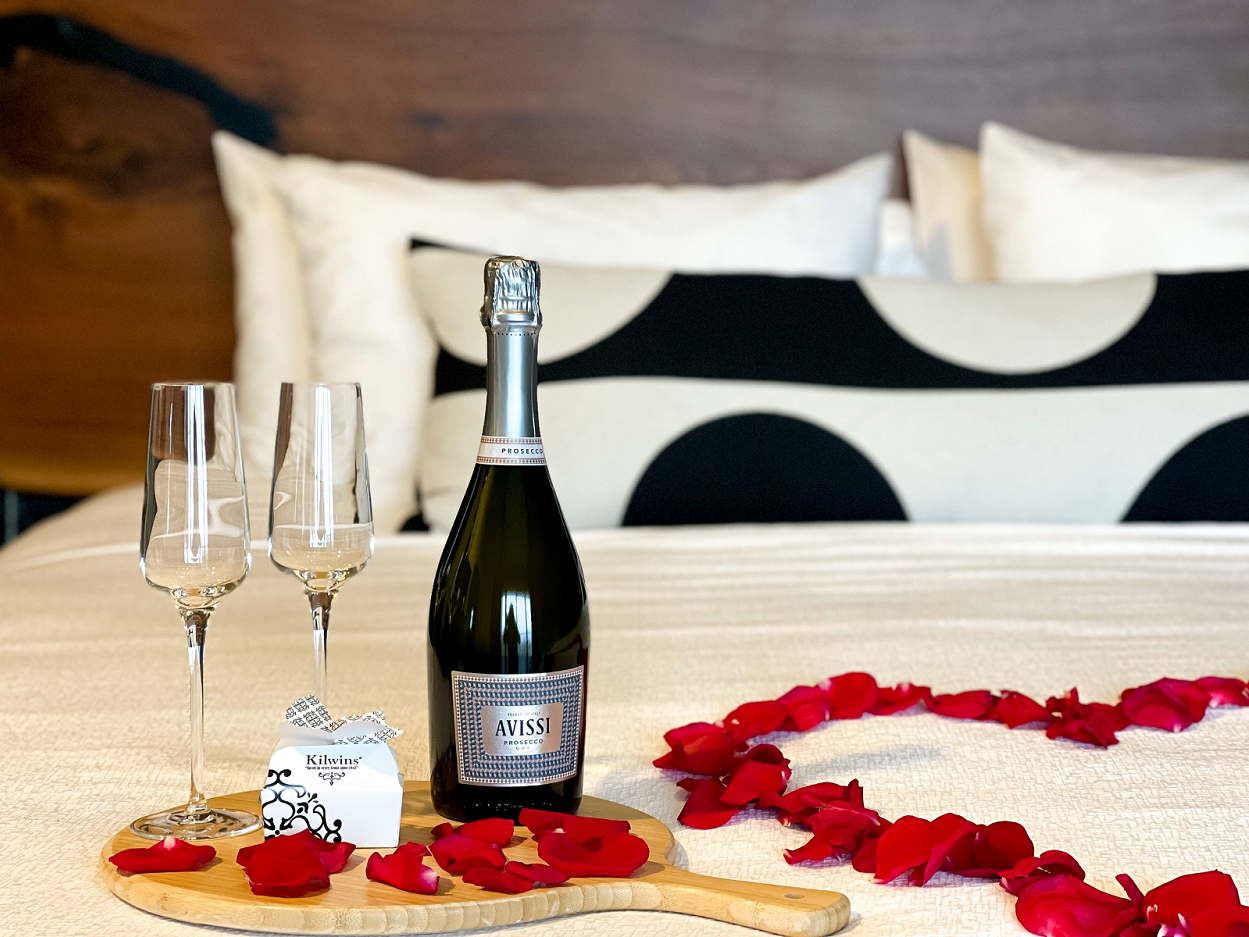 Prosecco champagne, two wine glasses, chocolates and rose petals on the bed