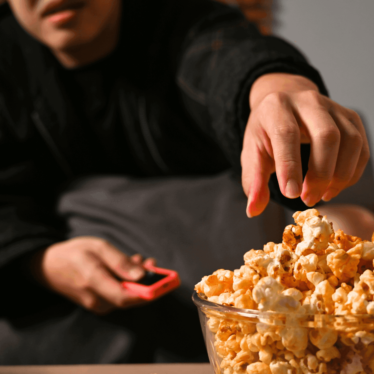 A hand reaching into a clear bowl of popcorn