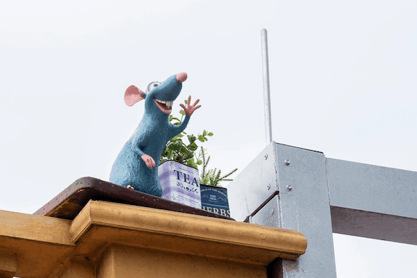A smiling gray mouse perched on a rooftop beside two containers of tea waves. 