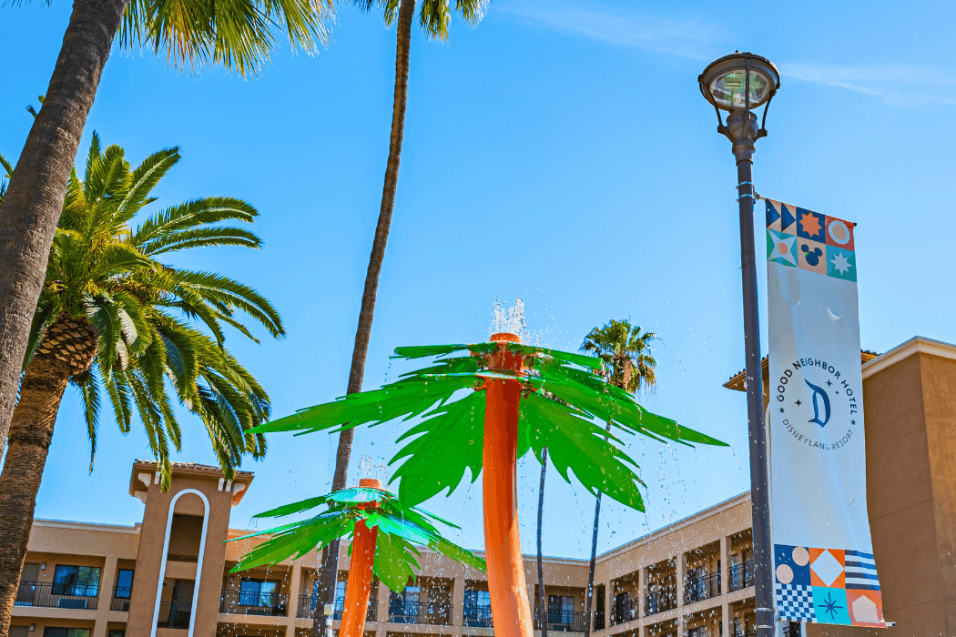 A low-angle shot of a hotel exterior with a water feature, palm trees, and a banner.