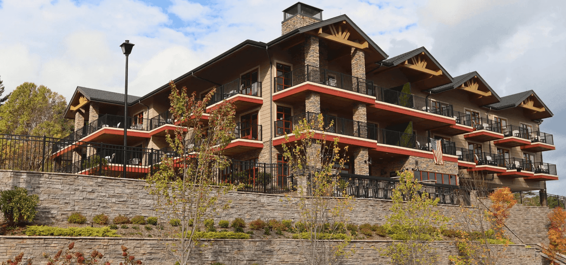 The Embers Hotel exterior with a stone facade, wood balconies and terraces, framed by pine trees and tiered gardens