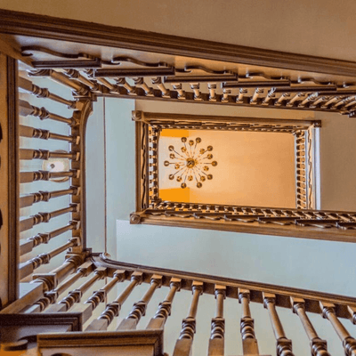 View looking up a grand spiral staircase at The Exeter Inn, featuring a decorative chandelier and intricate wooden railings