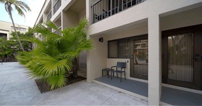 Ground floor patio with a blue chair and side table beside glass doors and lush tropical palm trees at Miami Lakes Hotel