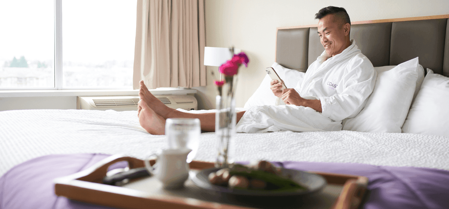 man sits in bed with Coast Hotels robe and room service tray