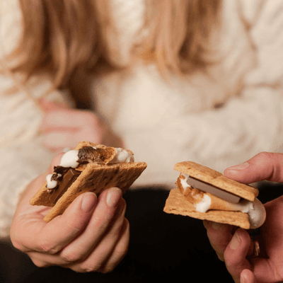 Two guests holding freshly made s\'mores with melted marshmallows and chocolate at La Tourelle Hotel and Spa
