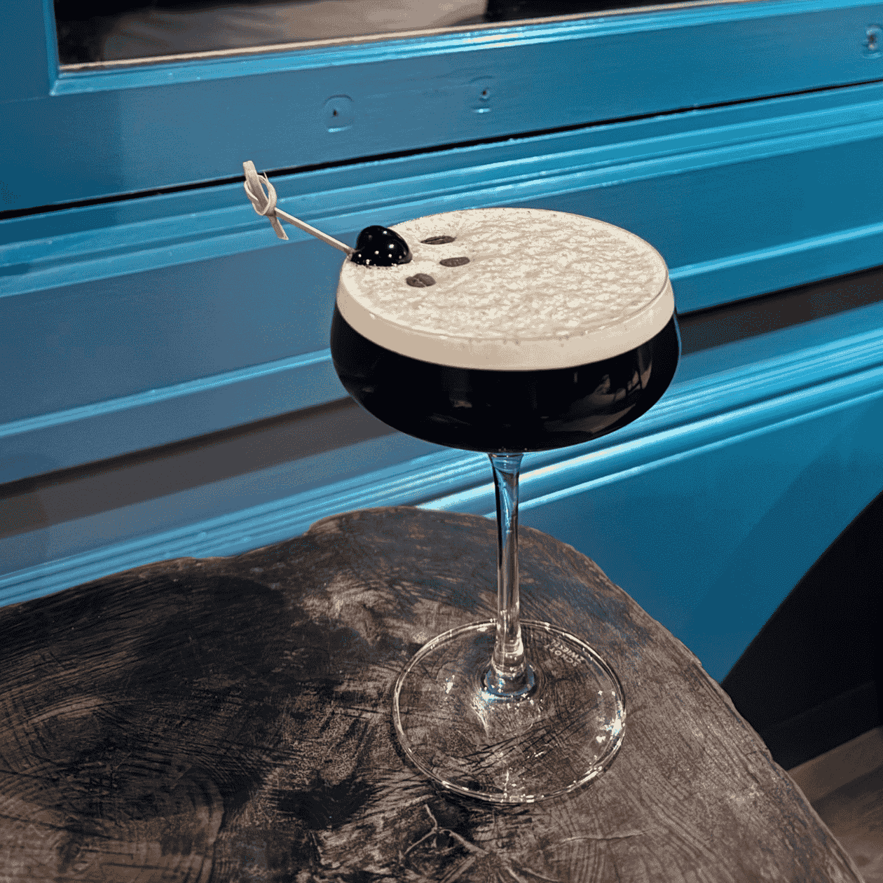 Cocktail glass with black drink and white foam, garnished with a black olive at The Stonebreaker.