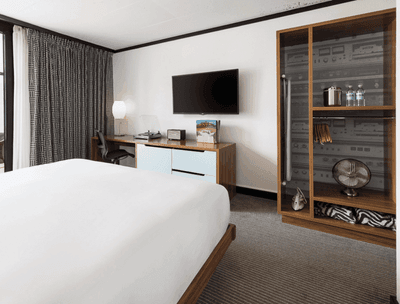King-size bed, work desk, a TV, and a wooden cupboard in Accessible King - Roll-In-Shower at The Verb Hotel
