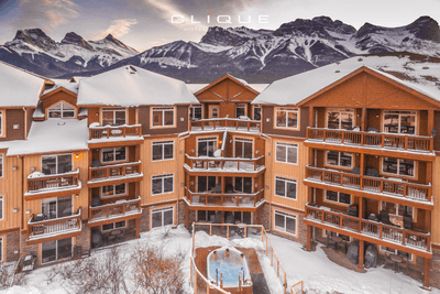 Aerial view of snow-covered Falcon Crest Lodge nestled amidst towering, snow-capped mountains under a dramatic sky