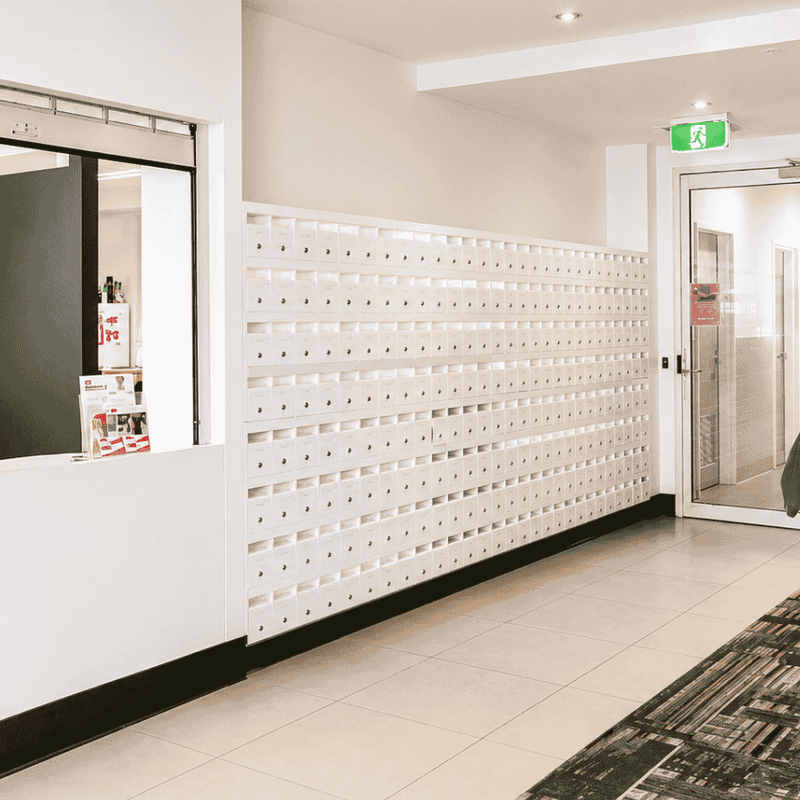 Modern reception area with white service counter, mailbox wall, tiled flooring, and potted plant at Student Living - Waymouth