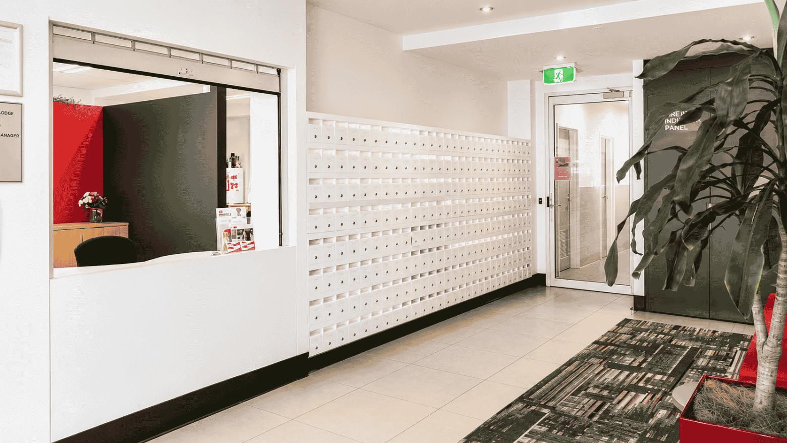 Modern reception area with white service counter, mailbox wall, tiled flooring, and potted plant at Student Living - Waymouth