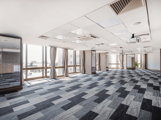 An empty room with grey and black patterned carpet, glass walls, and a white ceiling with recessed lighting.