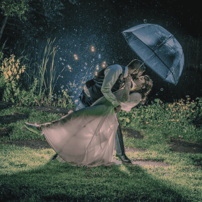 Bride and groom sharing a kiss beneath an umbrella on the lawn during a nighttime wedding at La Tourelle Hotel and Spa