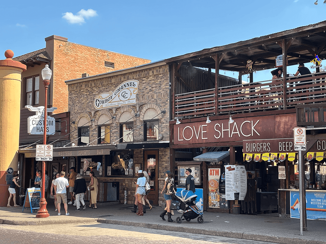 Fort Worth Stockyards with People walking by a burger shack under a wooden balcony near Warwick Melrose Dallas
