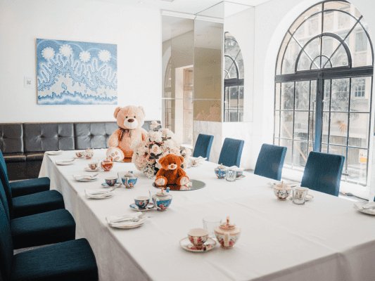 Blue chairs around a white table set with teapots and teddy bears.