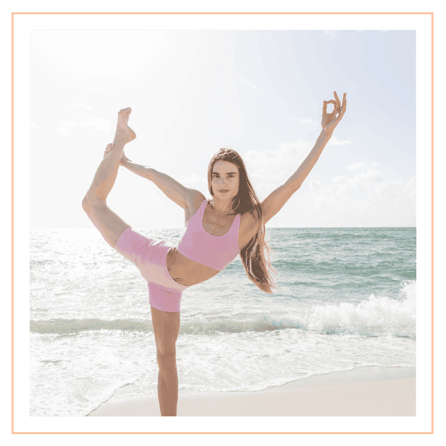 A woman in pink activewear holds a King Dancer yoga pose on the sandy beach near The Plymouth Hotel South Beach