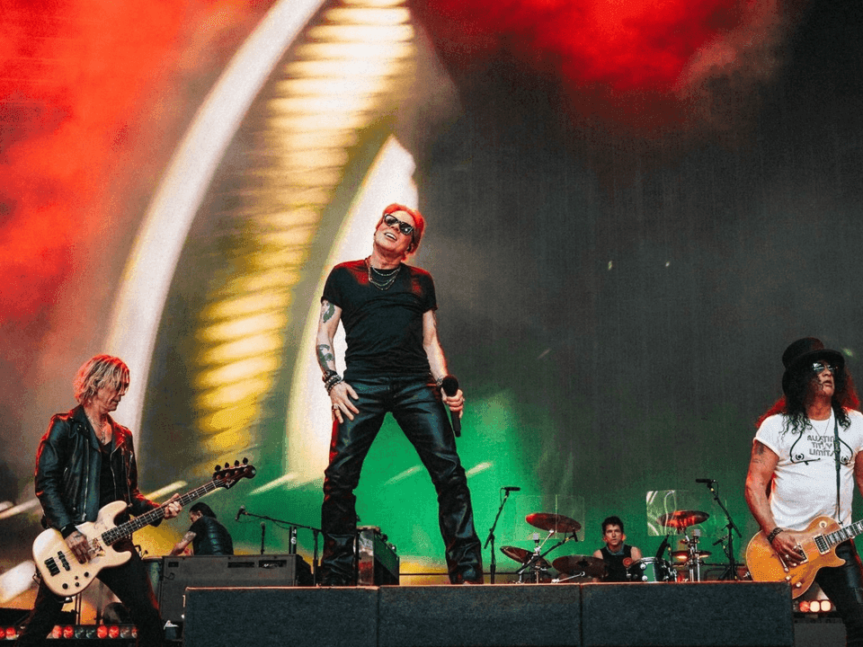 Guns N' Roses performing on stage with guitars and dynamic background visuals.