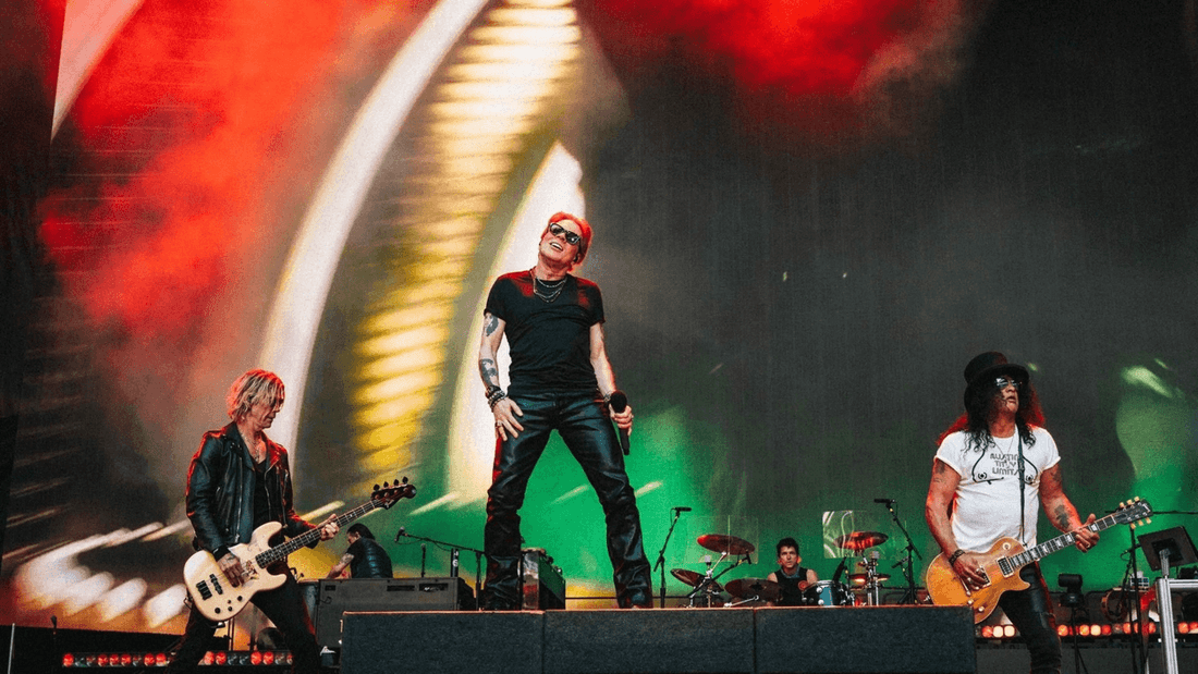 Guns N' Roses performing on stage with guitars and dynamic background visuals.