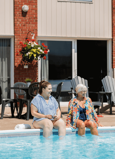 Two women dangling their feet in the outdoor swimming pool near the patio lounge chairs at Rodd Moncton