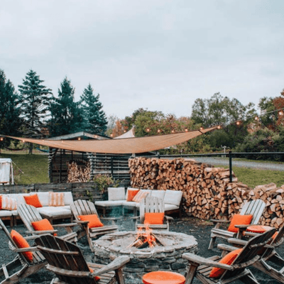 Outdoor stone fire pit surrounded by wooden chairs with cushions beside firewood at La Tourelle Hotel and Spa