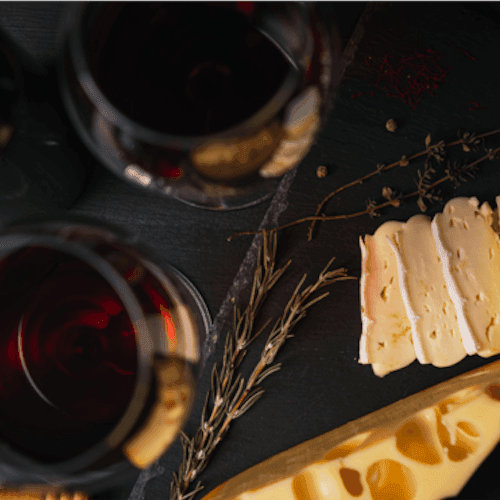 Glasses of wine with cheese slices on a dark surface for Summer Wine and Cheese Pairing.