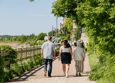 Guests walking along a paved waterfront nature path lined by green foliage and a wooden railing outside the Rodd Moncton