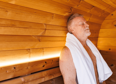 Man resting peacefully with a white towel around his neck along the warm wood paneling in the sauna at Rodd Moncton