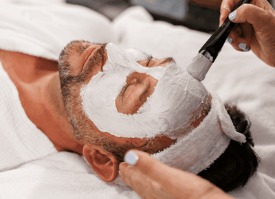 Man receiving a facial mask treatment by a therapist while resting on a spa bed at Rodd Crowbush Golf & Beach Resort