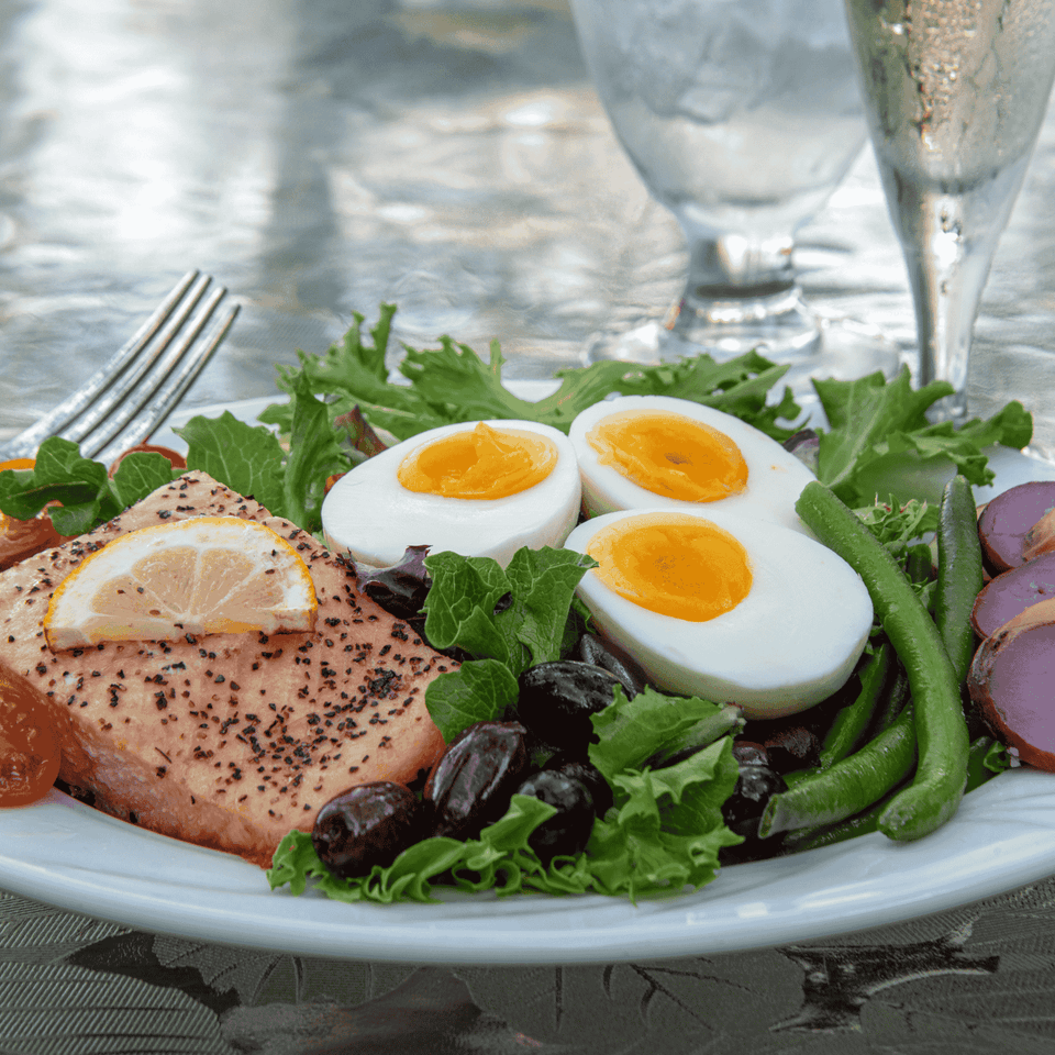 Nicoise salad with soft-boiled eggs, seared salmon, and olives with lemon wedges and wine glasses at La Tourelle Inn & Spa