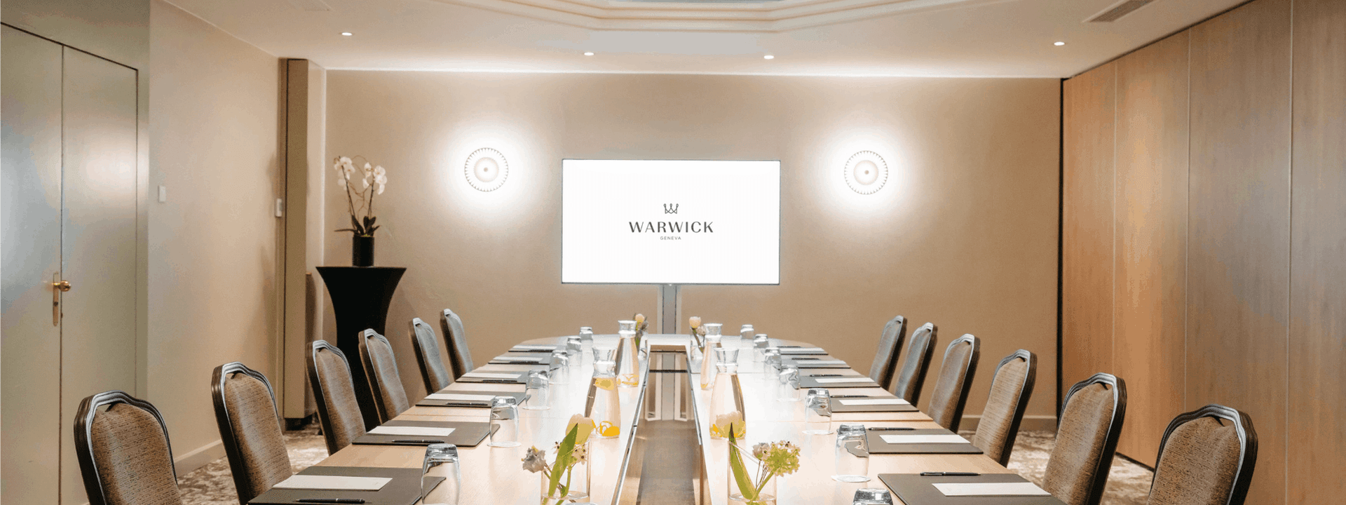 Oval boardroom table surrounding central flowers with a glowing screen in Dent-Blanche at Warwick Geneva