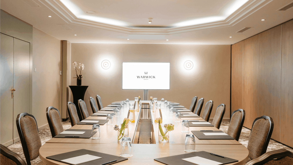 Oval boardroom table surrounding central flowers with a glowing screen in Dent-Blanche at Warwick Geneva