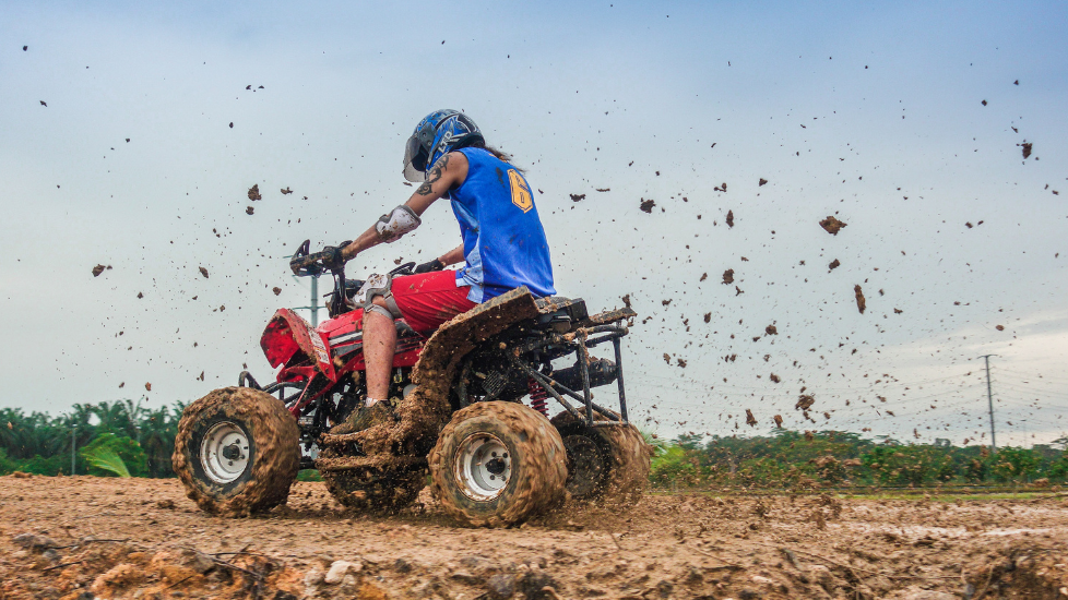 A person riding an ATV through muddy terrain, splashing mud around near Sunway Hotel Big Box
