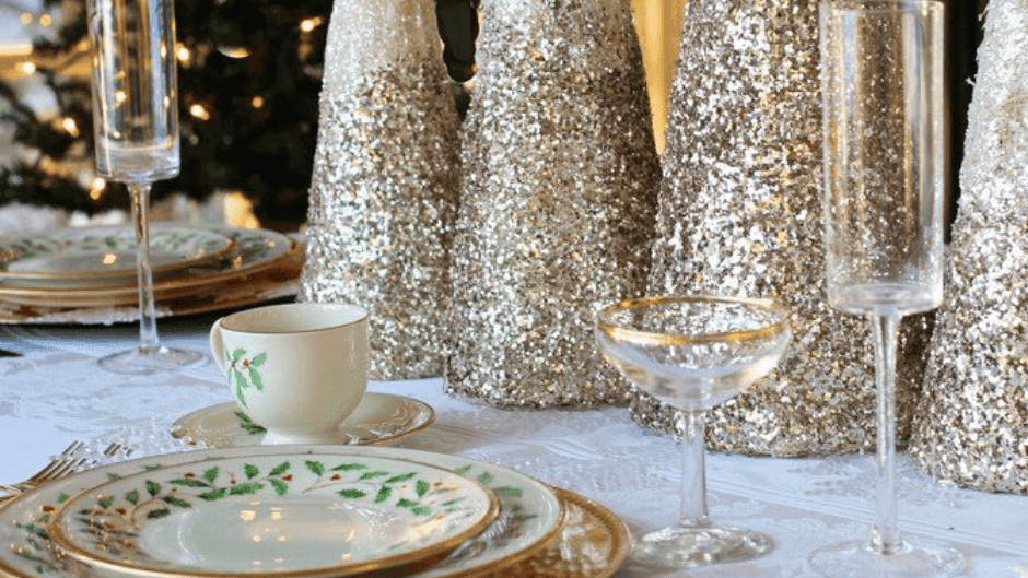Vaisselle et verres élégants sur une table de fête avec des arbres scintillants en arrière-plan.
