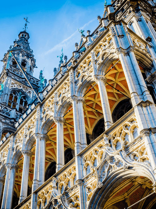 Historisch stadhuis met sierlijke gotische architectuur en verlichte bogen tegen een blauwe hemel in Brussel.