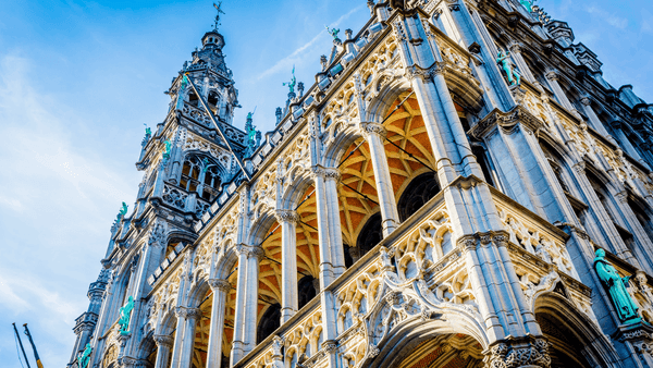 Façade ornée d'un bâtiment historique avec arcades gothiques et tour décorative sous un ciel bleu à Bruxelles