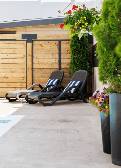 Two black chaise lounge chairs with striped pillows under hanging flowers beside a swimming pool at the Rodd Moncton