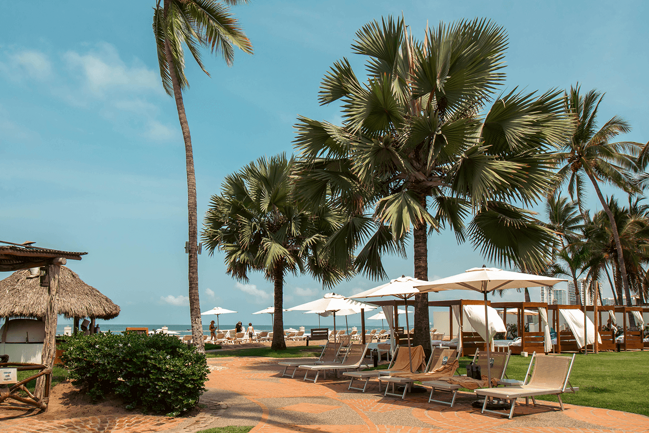 Lounge chairs by the pool surrounded by palm trees at Plaza Pelicanos Grand Beach Resort
