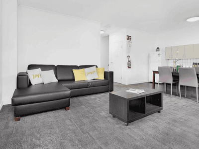 Modern open-plan living area with gray sectional sofa, dining table, and kitchen at Springfield Central