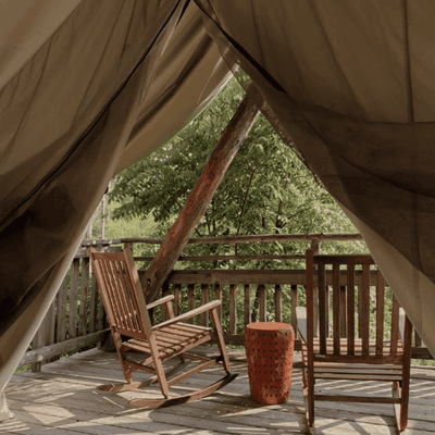 Two wooden rocking chairs on a covered porch deck viewed from inside a glamping tent at La Tourelle Hotel and Spa