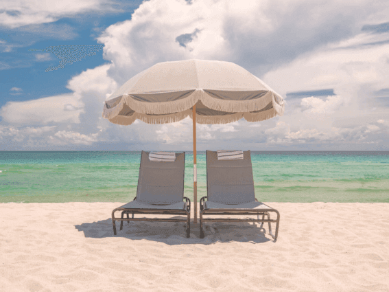 Two grey loungers with towels sit beneath a fringed white umbrella on the sandy beach near The Plymouth Hotel South Beach