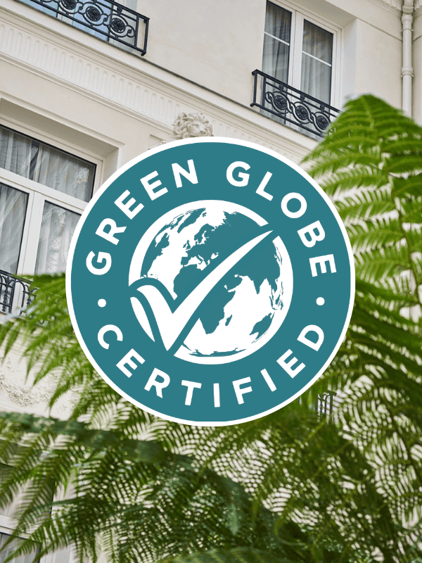 Green Globe Certified badge displayed with lush ferns in front of an elegant Parisian hotel facade with ornate balconies.