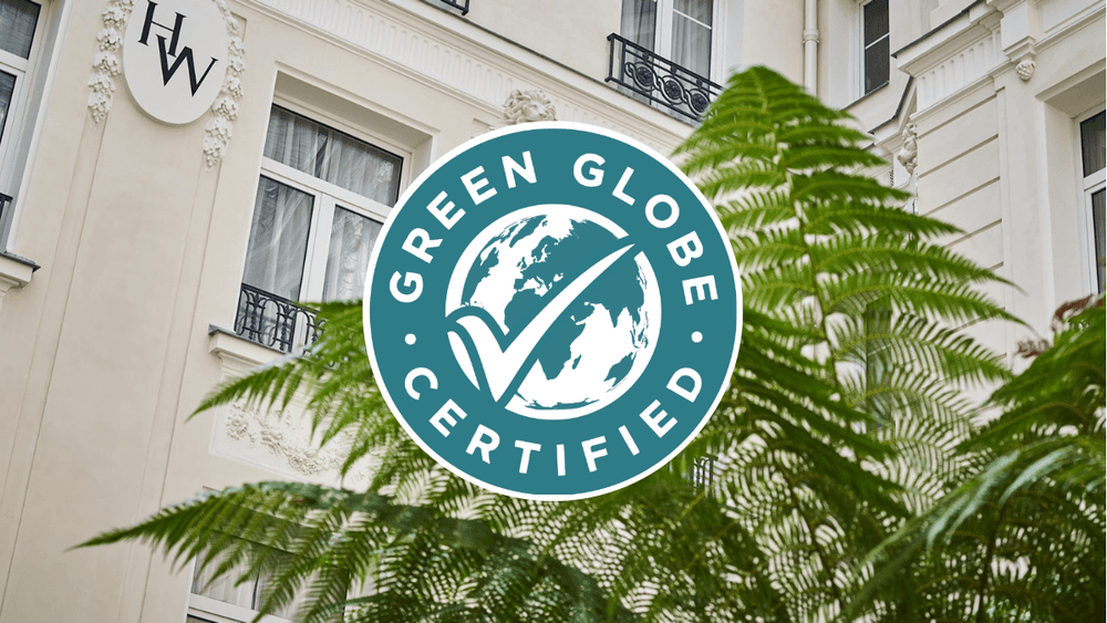 Logo de certification Green Globe devant la façade élégante d'un hôtel parisien avec végétation luxuriante au premier plan