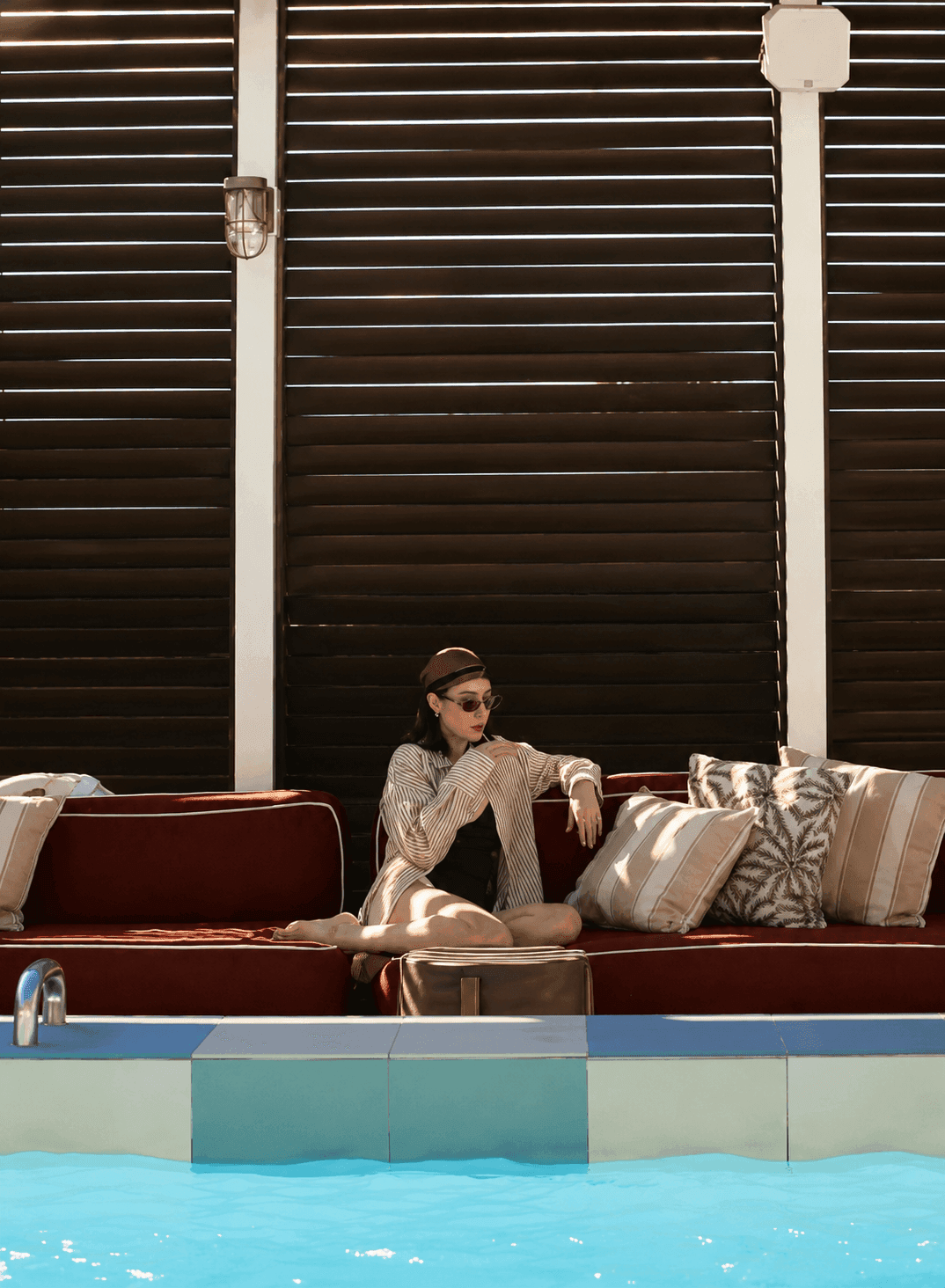 A woman sits on a red couch next to a pool.